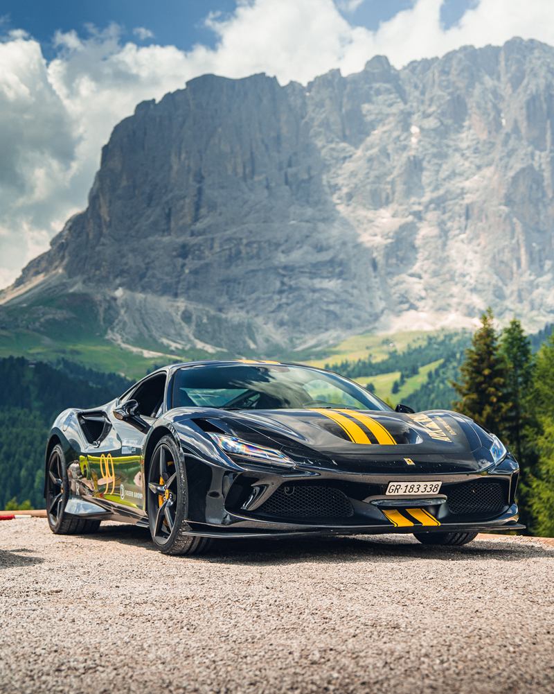 Black Ferrari with yellow stripes below a Dolomites peak