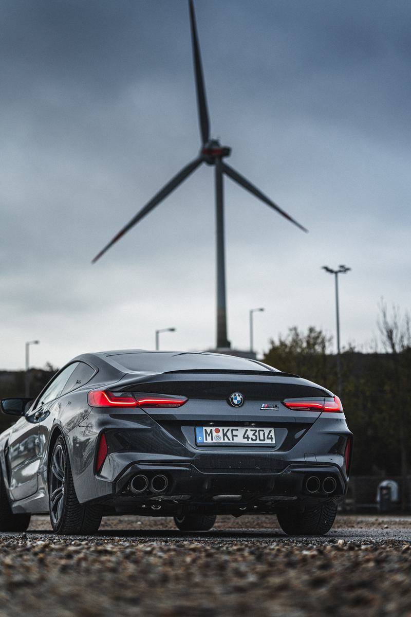 Grey BMW below a wind turbine and a stormy sky